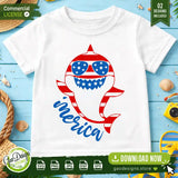 A white kids holiday t-shirt mockup displaying the vertical American flag striped shark wearing star-patterned sunglasses with blue script text reading Merica, set against a summer beach themed background.