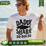 A smiling man at the beach holding a surfboard, wearing a white t-shirt featuring the Daddy Shark Do-Doo-Do SVG design. A perfect summer lifestyle mockup showcasing trending Father's Day apparel ideas for print-on-demand businesses.