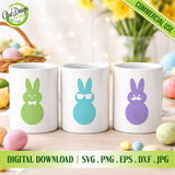 Three white mugs with colorful bunny designs on a table with Easter eggs and flowers.